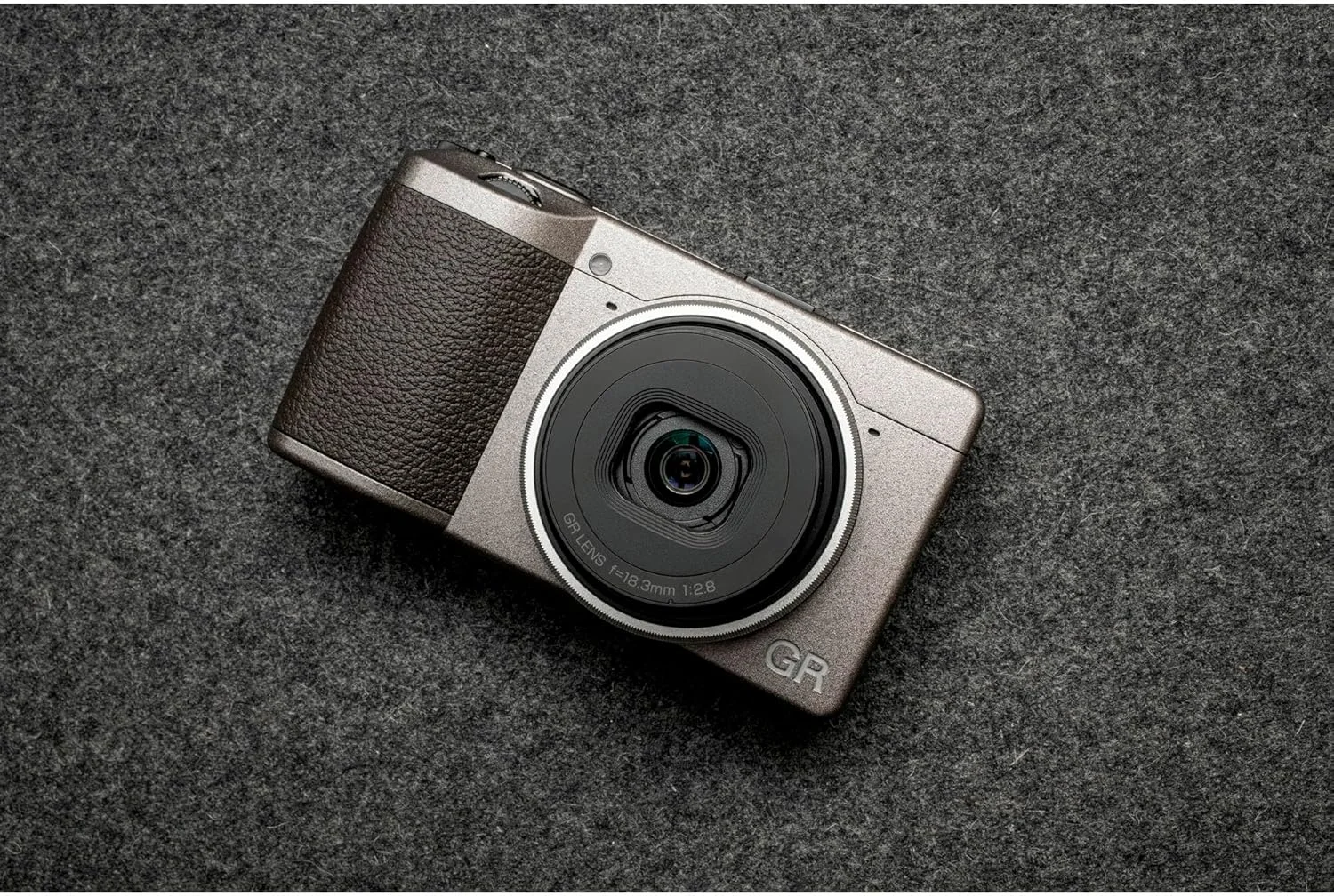 دوربین کامپکت دیجیتال Ricoh GR III Diary Edition، بدنه خاکستری-گرم متالیک با گریپ قهوه‌ای تیره و حلقه نقره‌ای طبیعی، با سنسور CMOS سایز APS-C 24 مگاپیکسلی، لنز 28mmF2.8 GR (در فرمت 35mm)