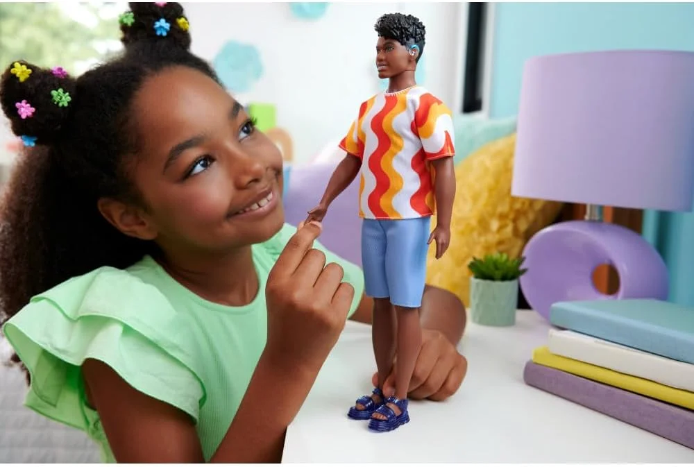 عروسک کن فشنista شماره 220 با سمعک پشت گوش و اندام درشت، با پیراهن طرح دار نارنجی، شورت و صندل ژله ای قابل تعویض