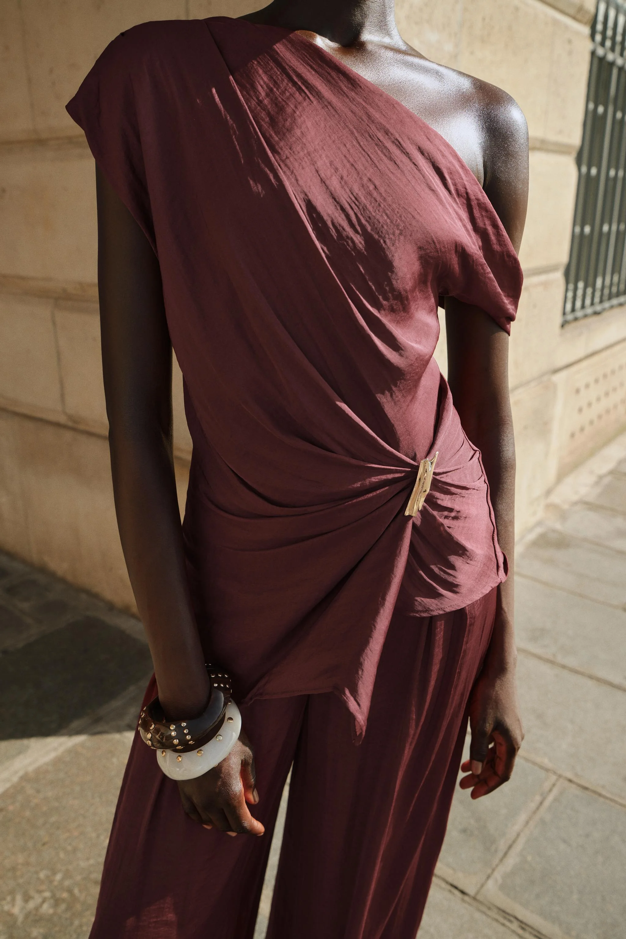 تاپ یقه روان با آستین های نامتقارن. جزئیات سخت افزاری طلایی رنگ در قسمت جلو.