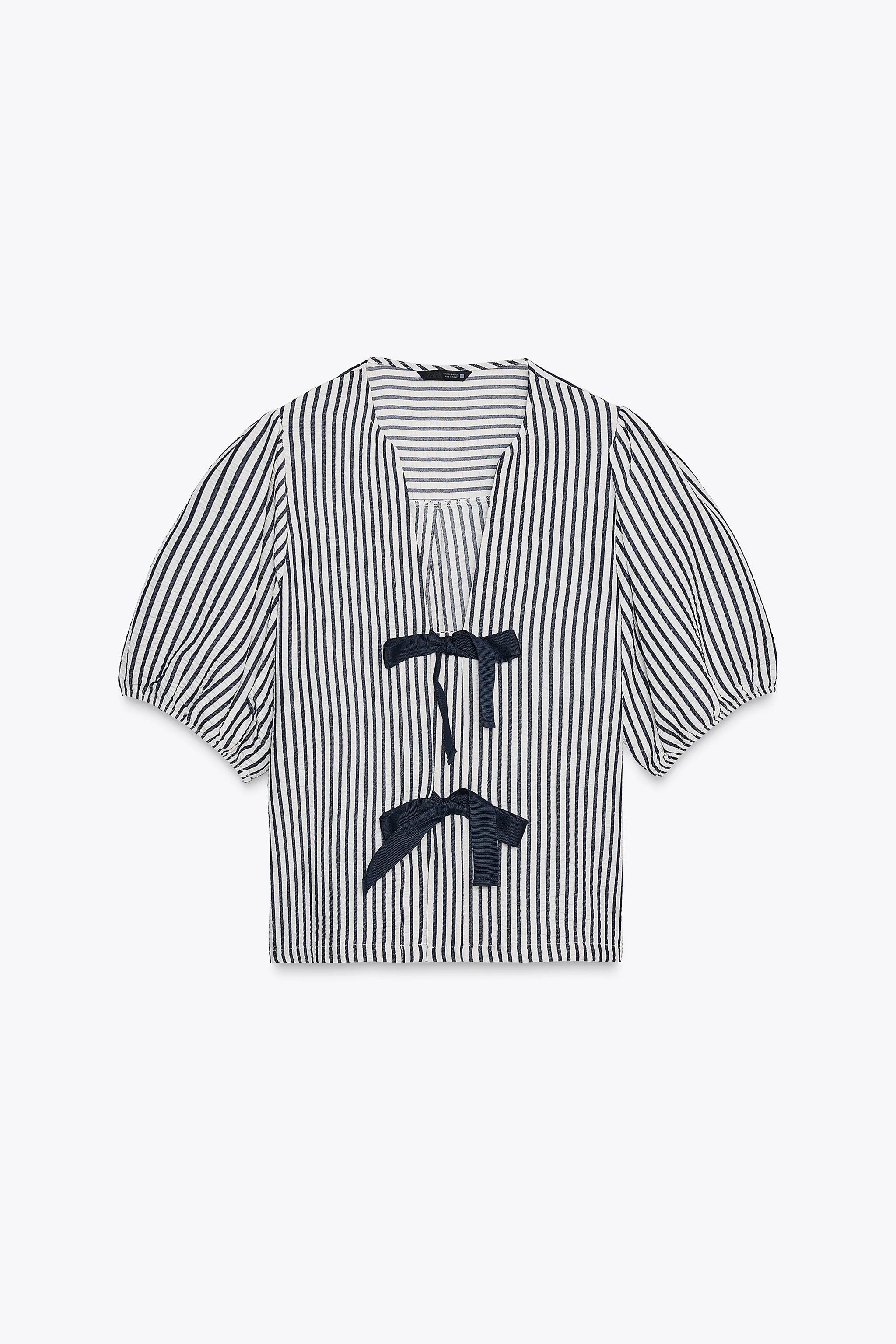 بلوز با ترکیب پارچه لینن. یقه گرد با برش هفت و آستین های کوتاه پفی با لبه کشی. دارای بند برای گره زدن در قسمت جلو.