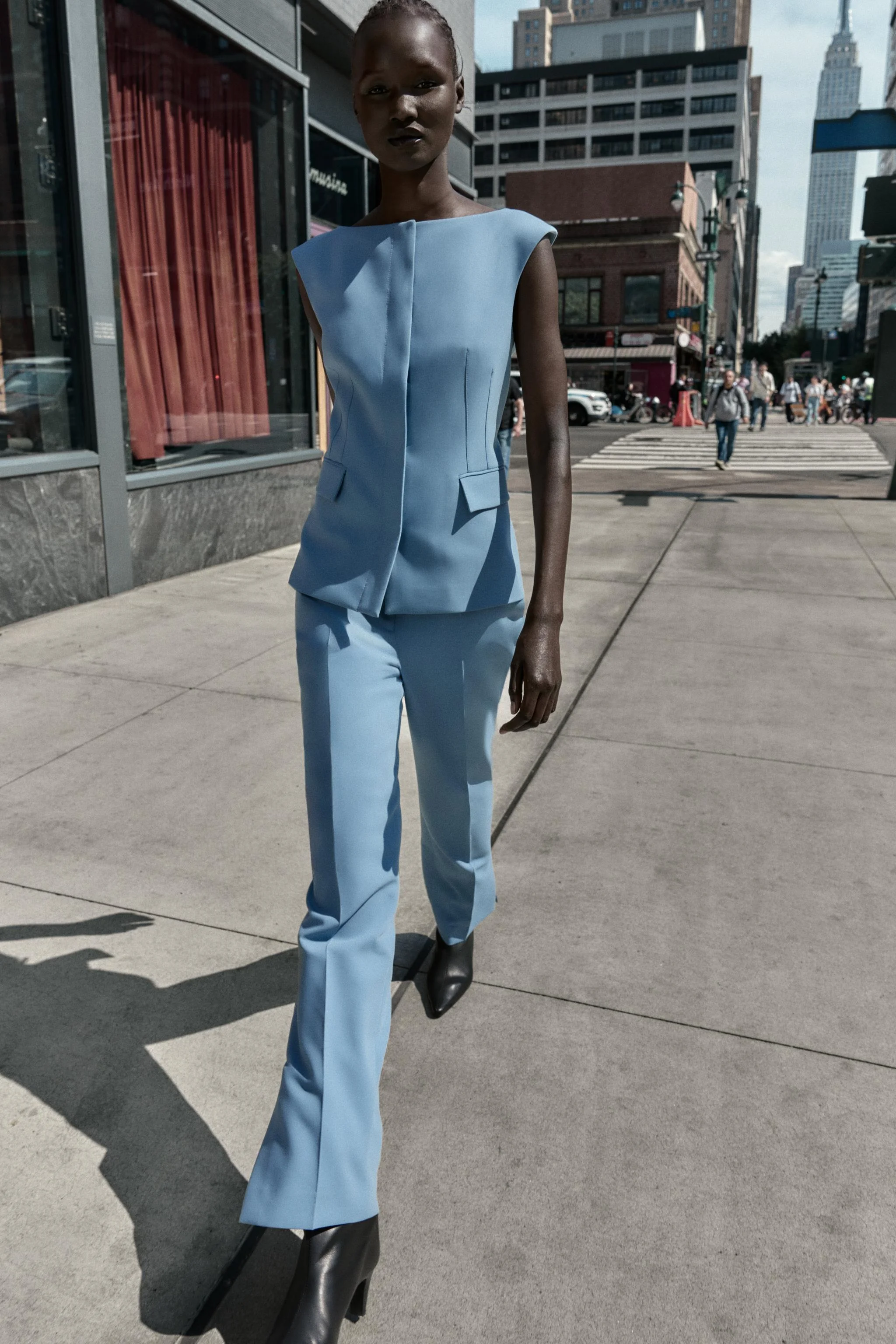 جلیقه فیت با یقه قایقی و طراحی بدون آستین. دارای جیب های پاکتی در جلو، چاک در لبه پشتی و بست دکمه فشاری مخفی در جلو.