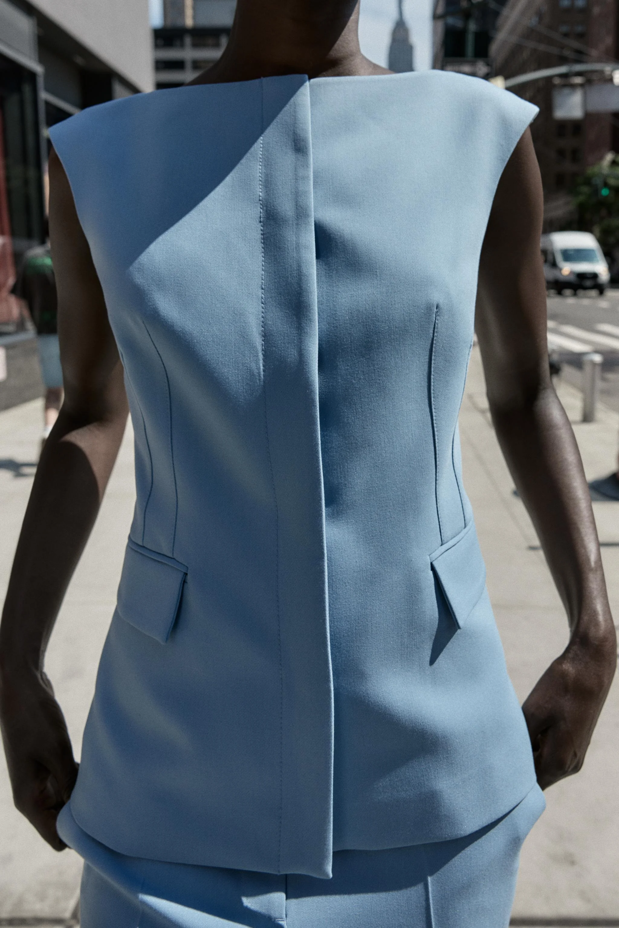 جلیقه فیت با یقه قایقی و طراحی بدون آستین. دارای جیب های پاکتی در جلو، چاک در لبه پشتی و بست دکمه فشاری مخفی در جلو.