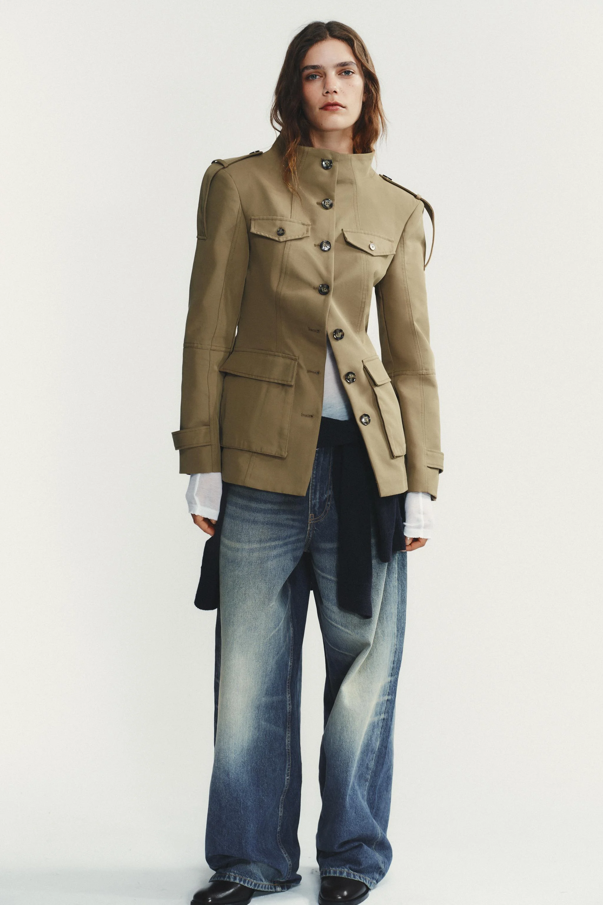 کت یقه ایستاده با آستین بلند و سرشانه‌های تزئینی. دارای جیب‌های پاکتی جلویی با دکمه و جزئیات دکمه روی سینه. دارای آستر. بسته‌شدن با دکمه در جلو.