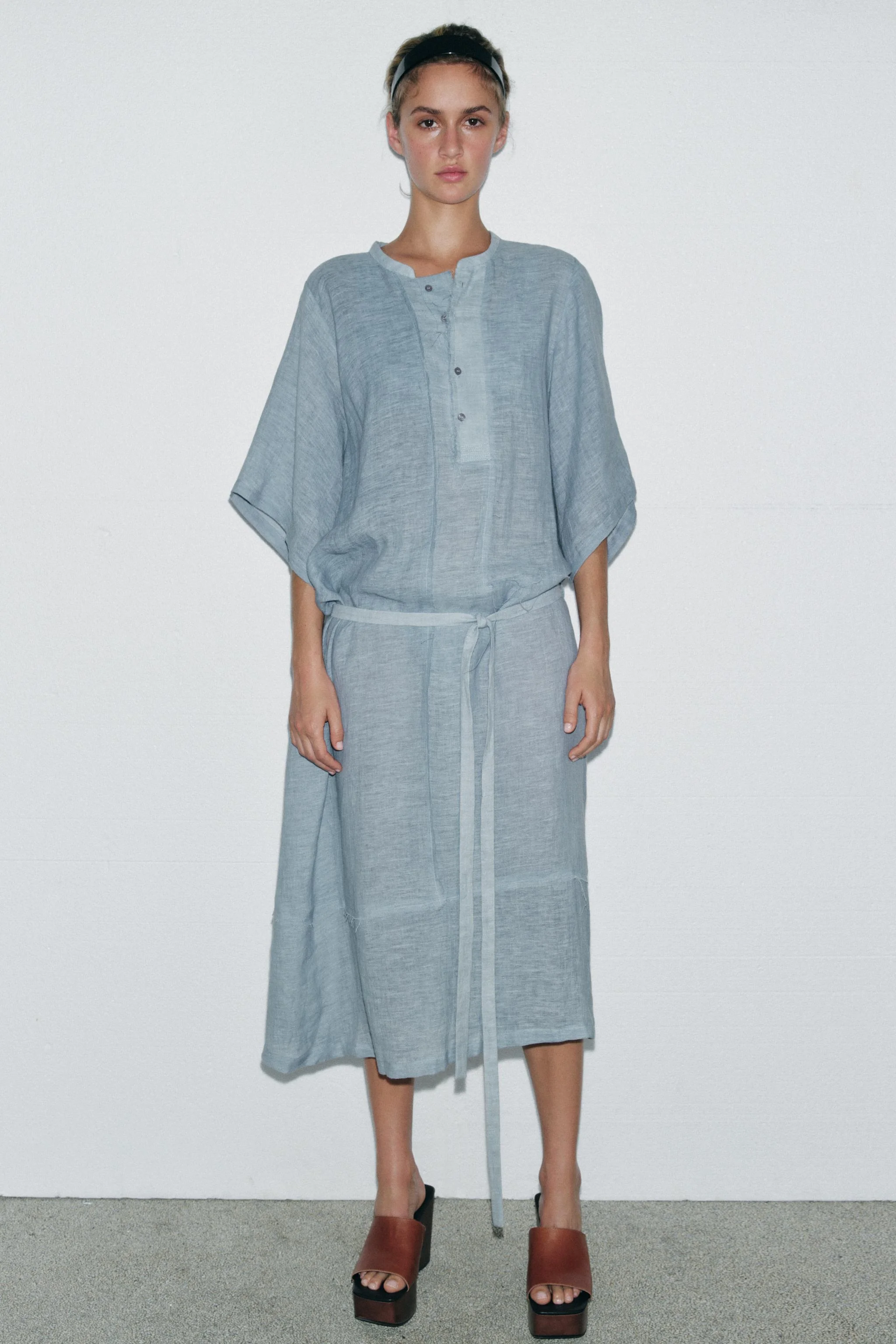 پیراهن میدی بافتنی ترکیبی از کتان، نسخه محدود. یقه گرد و آستین های سه ربع. دارای جزئیات پارچه ای با حاشیه های ریش ریش همرنگ. دارای کمربند. دکمه های جلوی لباس.