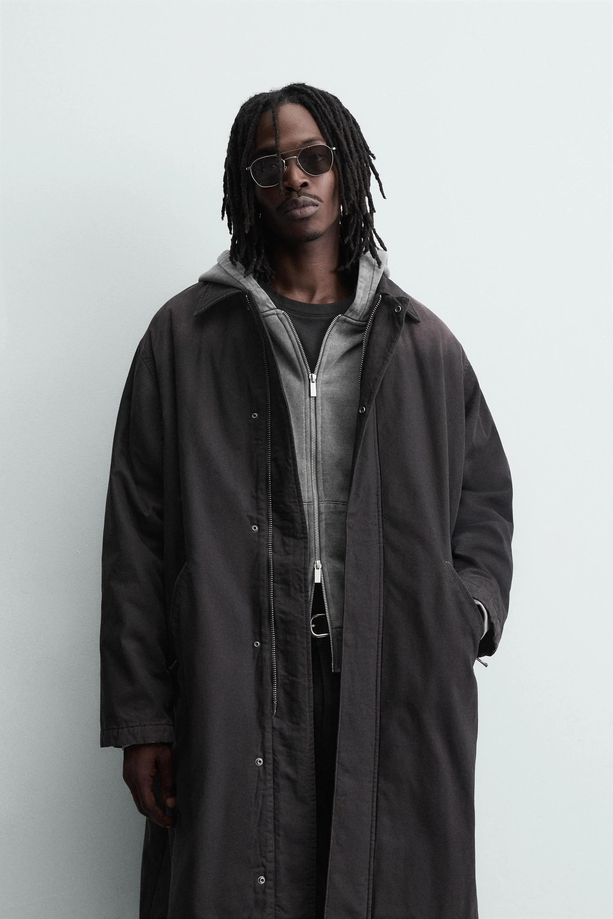 کت جین پنبه ای با تن خور راحت. دارای یقه برگردان و آستین های بلند با سرآستین های دکمه دار قابل تنظیم. دارای جیب های زیپی در قسمت جلوی باسن و یک جیب داخلی. دارای جلوه رنگ رفته. بستن جلوی کت با زیپ مخفی شده توسط یک سجاف دکمه دار.