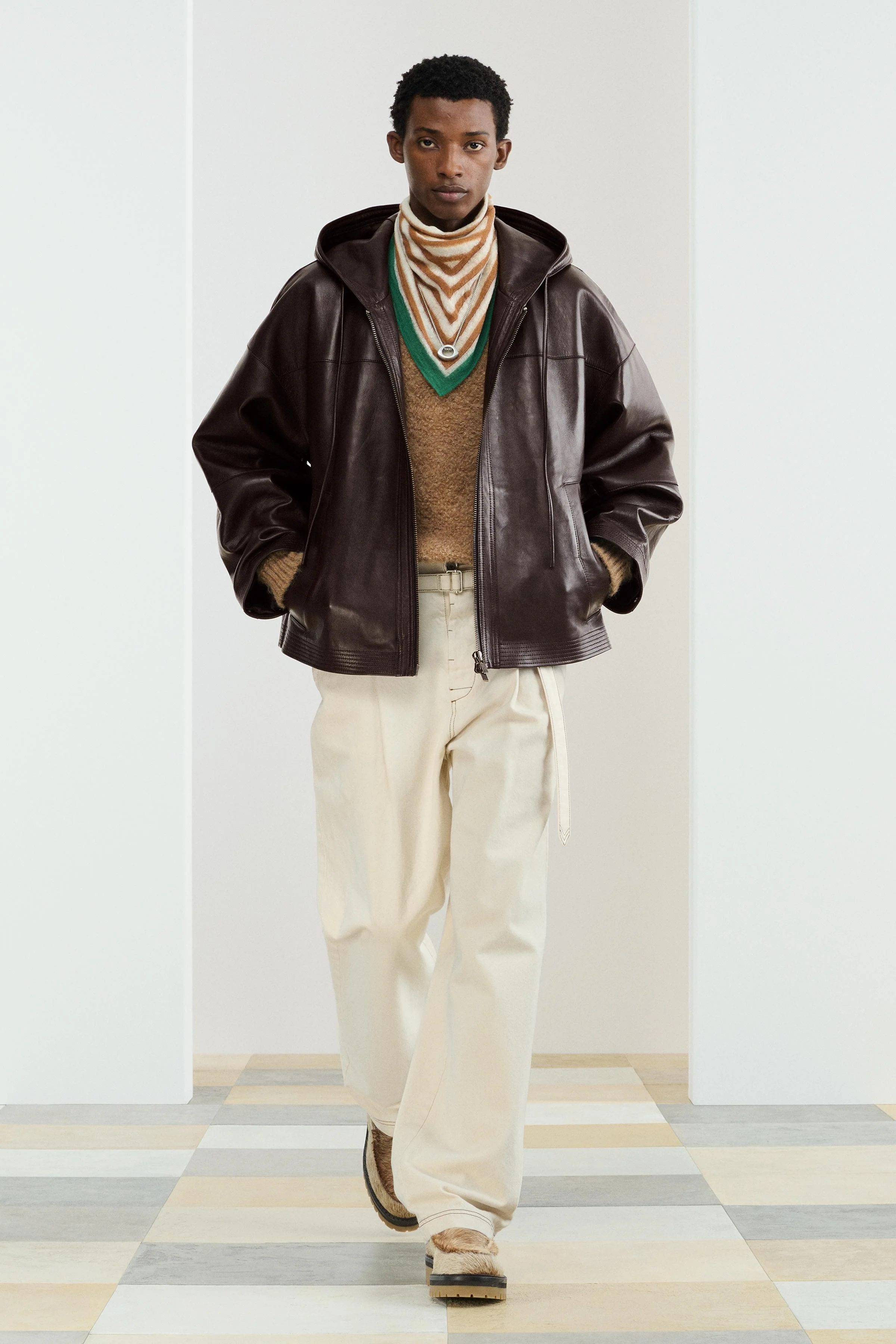 کت چرمی با تن خور آزاد. دارای کلاه قابل تنظیم. آستین های بلند با سرآستین های دکمه ای قابل تنظیم. جیب های مورب در طرفین و یک جیب داخلی. لبه پایین با دوخت همرنگ. دارای زیپ در جلو.