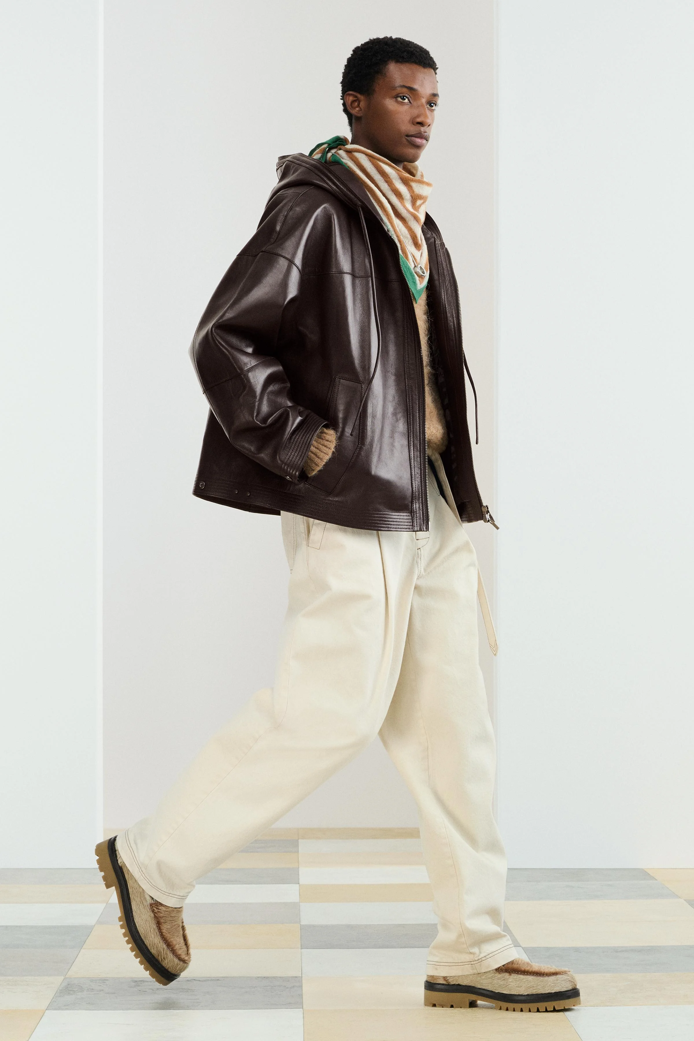 کت چرمی با تن خور آزاد. دارای کلاه قابل تنظیم. آستین های بلند با سرآستین های دکمه ای قابل تنظیم. جیب های مورب در طرفین و یک جیب داخلی. لبه پایین با دوخت همرنگ. دارای زیپ در جلو.