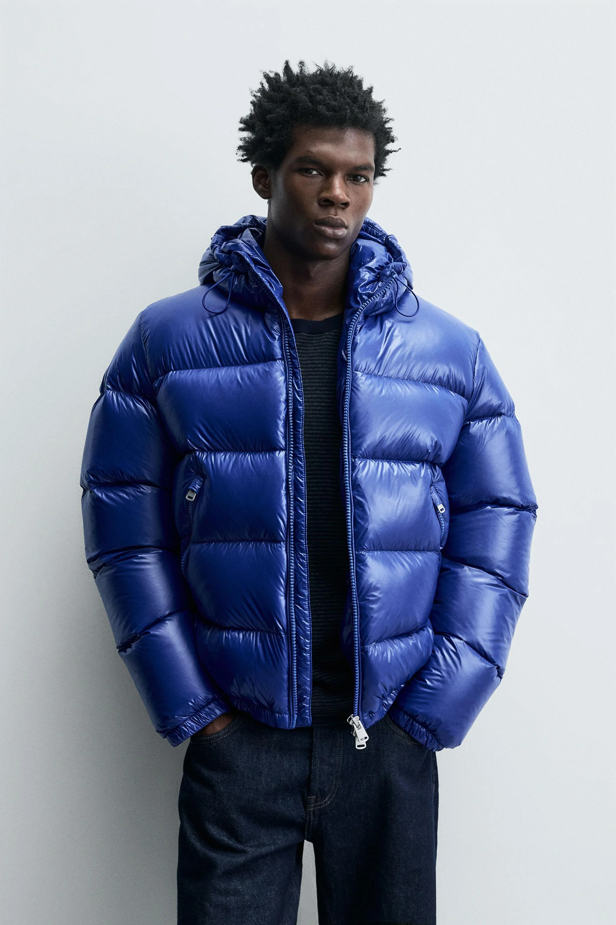 کاپشن پفی ساخته شده از پارچه فنی با روکش براق، دارای گردن بلند با کلاه قابل تنظیم، آستین های بلند با سرآستین های کشی، جیب های کناری و یک جیب داخلی. لبه پایین قابل تنظیم با کش در طرفین. دارای زیپ در جلو.